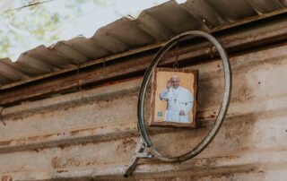 Um objeto circular está pendurado em uma parede de metal corrugado em Arniqueira, com uma placa de madeira com uma figura religiosa em seu interior.