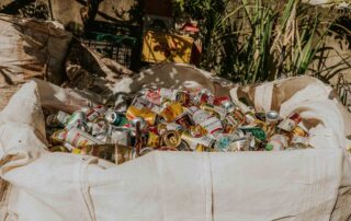 Um grande saco cheio de várias latas de alumínio vazias de refrigerante e cerveja fica ao ar livre em Arniqueira.