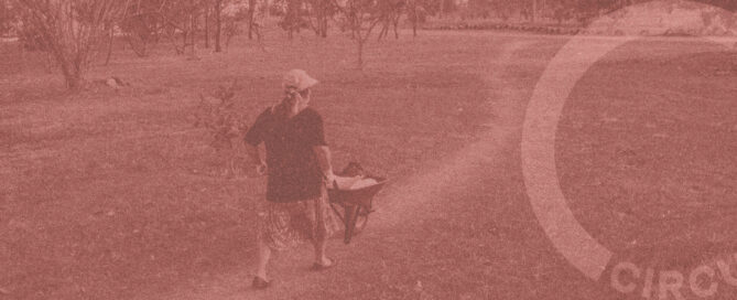 Uma pessoa é vista empurrando um carrinho de mão por um caminho em um parque, cercado por grama e árvores exuberantes. A imagem, com seus tons sépia vintage, transmite sutilmente a essência de "lançamento", já que a palavra CIRCULARIDADES é parcialmente visível no lado direito.